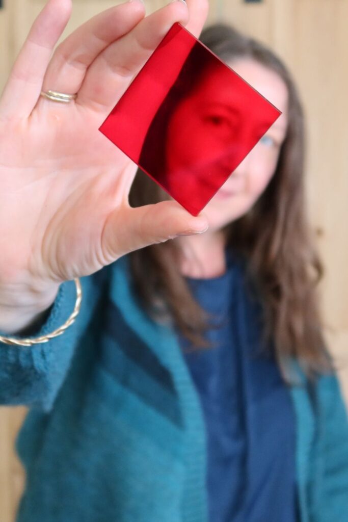 Woman holding red perspex square, reflecting her face, for choosing yarn colours