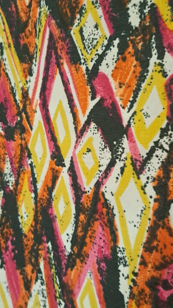 Althea McNish textile with obscure diamond shapes in charcoal, orange, pink and yellow.