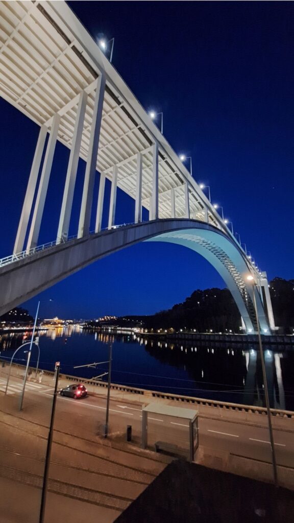Dark night sky with an arched bridge in Porto with city lights.