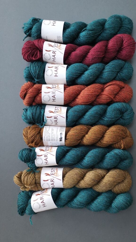Many skeins of yarn lined up in dark teal, rust, mid ornage and dirty yellow.