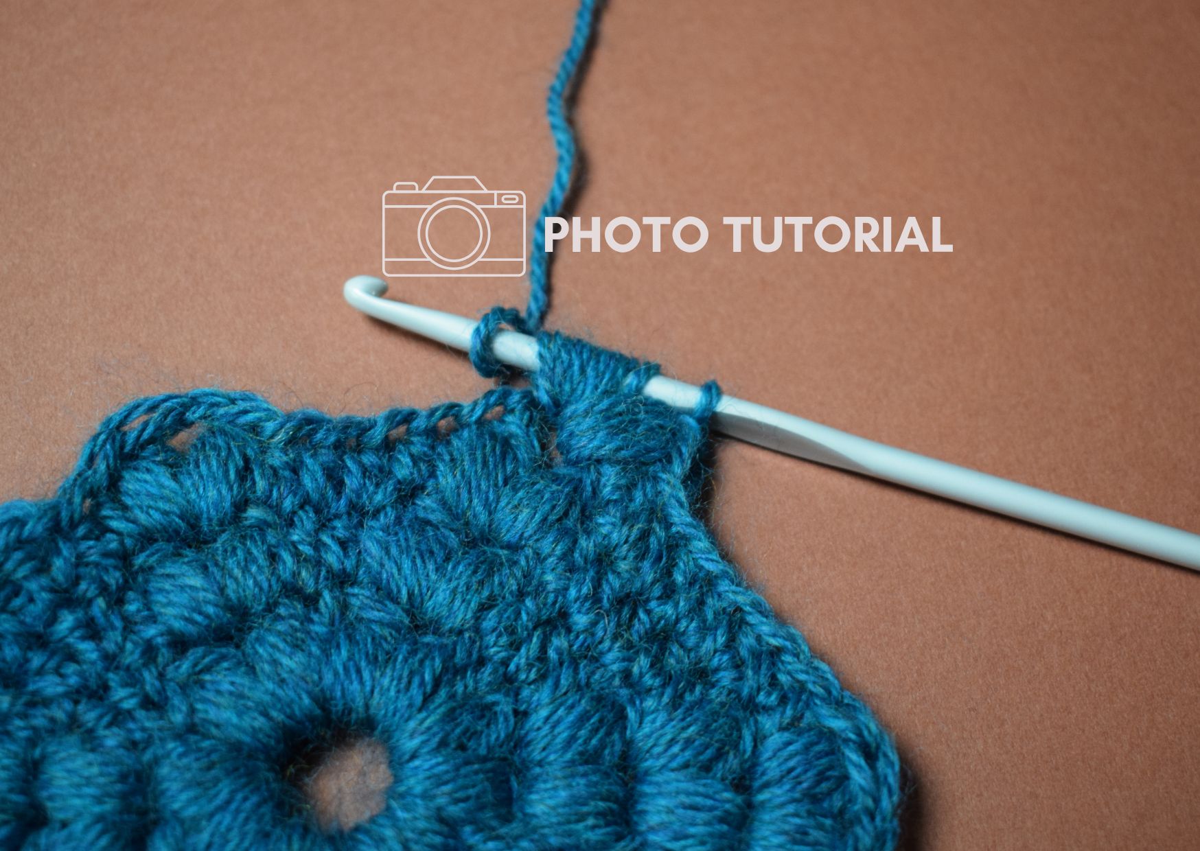 Teal crocheted hexagon motif with hook making a puff stitch.