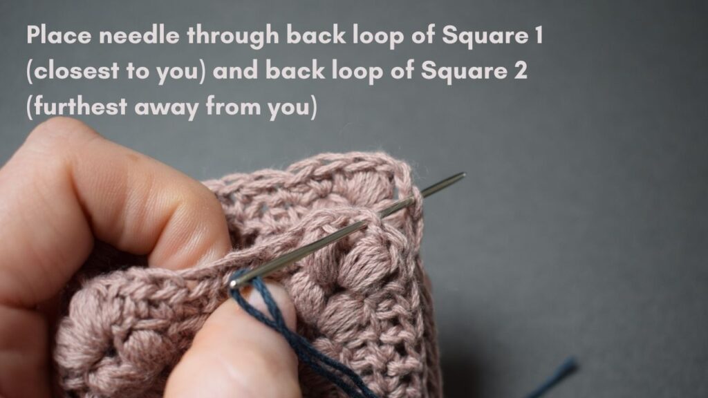 Two pink crocheted squares with right sides facing and a tapestry needle through the corner chains.