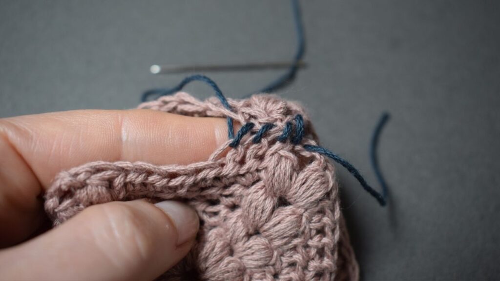Close up of two pink crocheted squares with right sides facing, being whip stitched together.