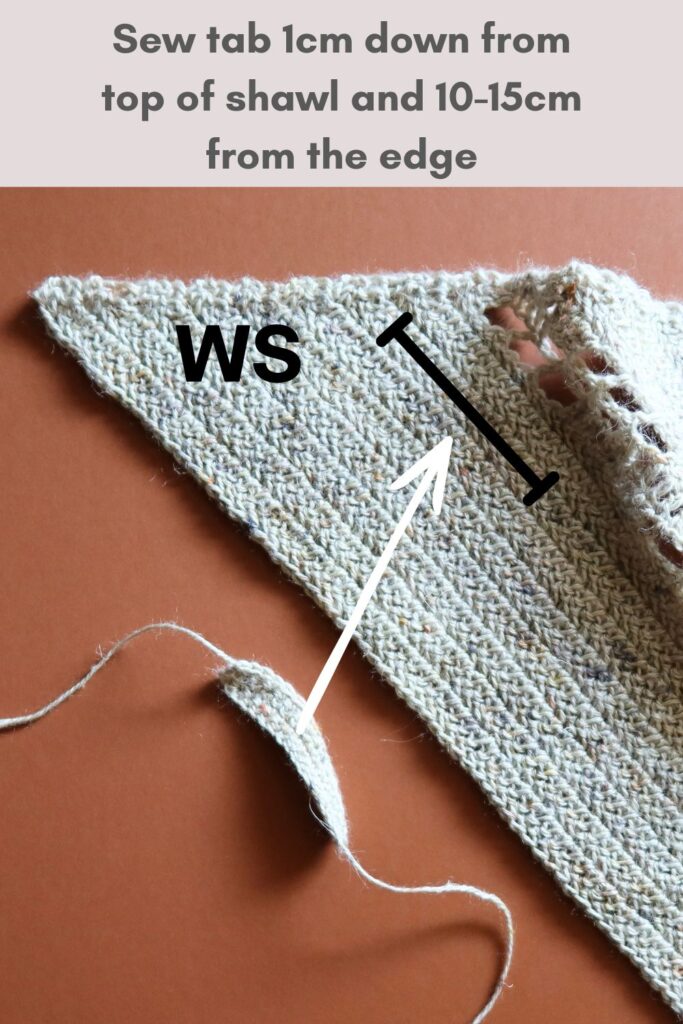 Close up of a crocheted shawl with a small tab to feed the shawl end through.