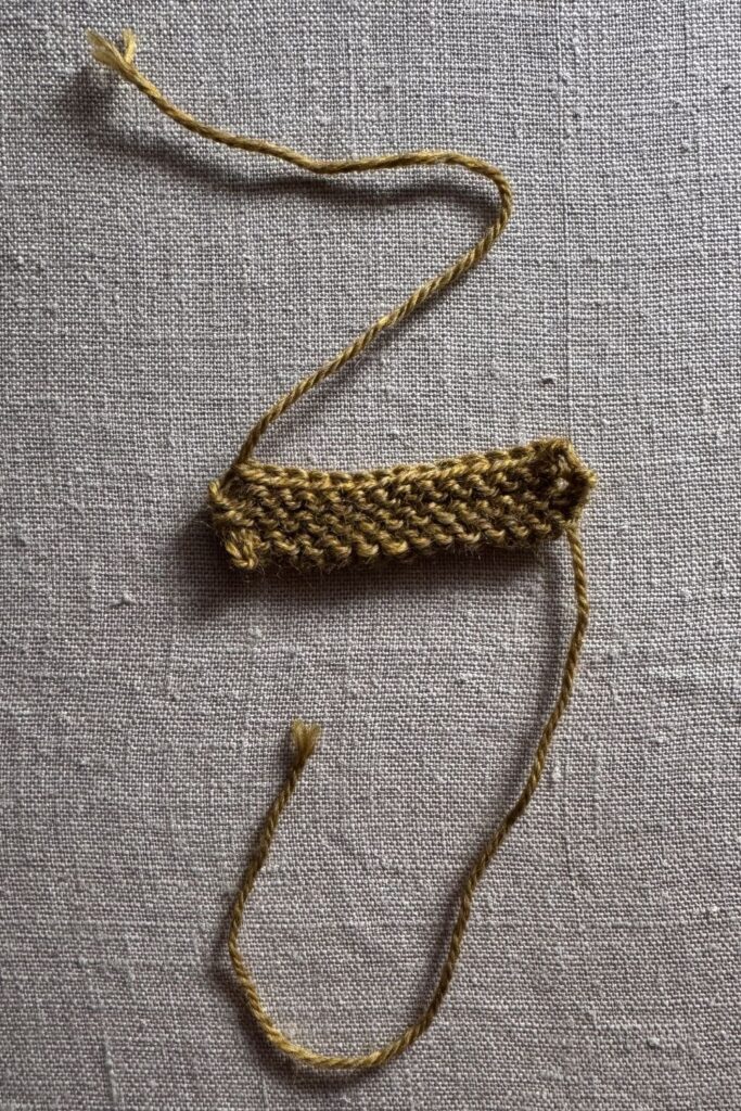 Close up of a knitted tab ready to be sewn onto a shawl to secure it while wearing.