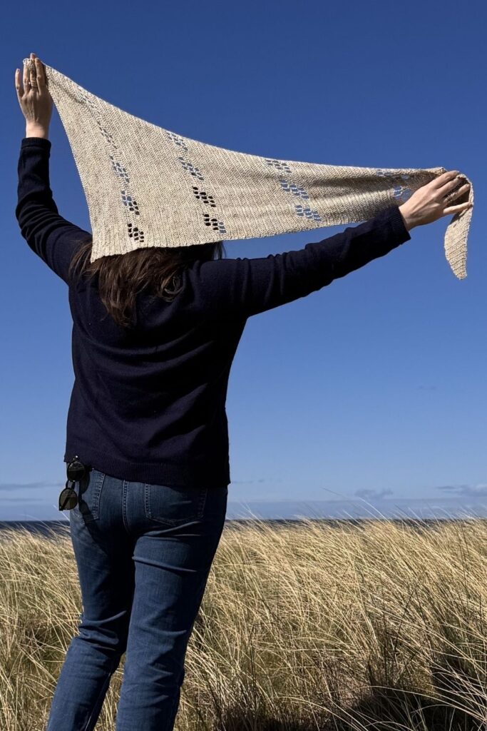 Asymetric triangle crochet filet shawl being held up high against a blue sky.