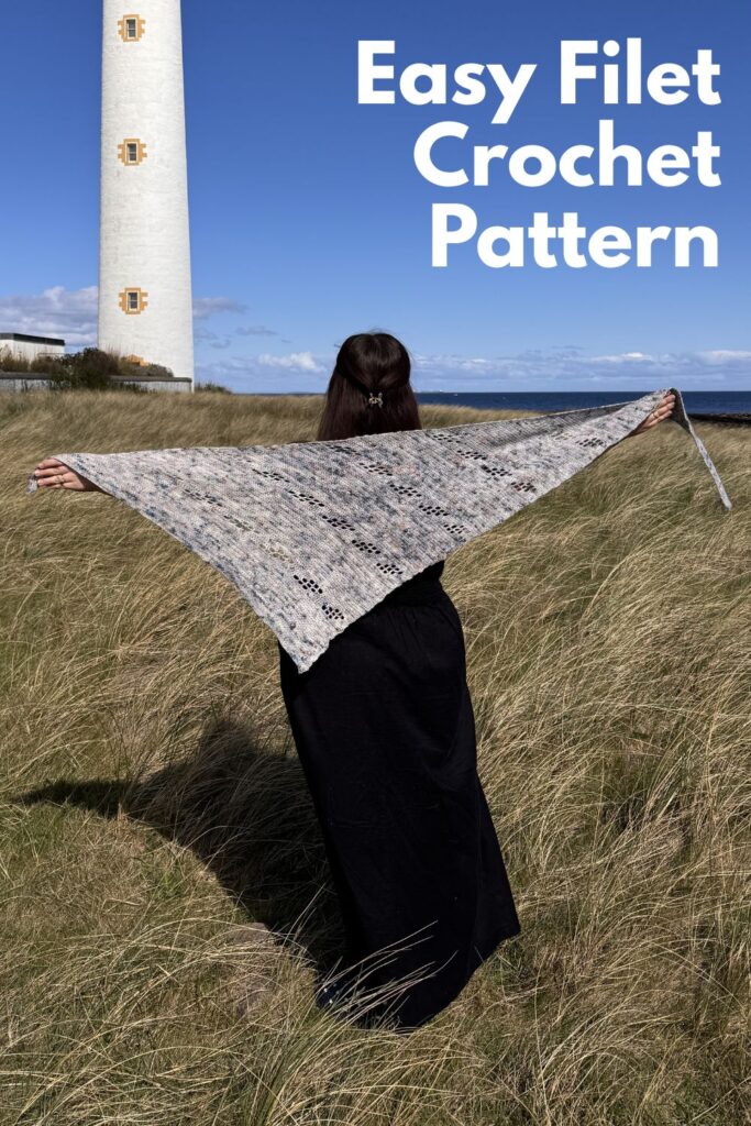Asymetric triangle crochet filet shawl being held up high against a blue sky.