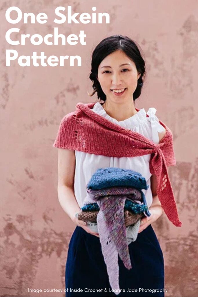Asymetric triangle crochet filet shawl being worn whilst holding a pile of other shawl samples.