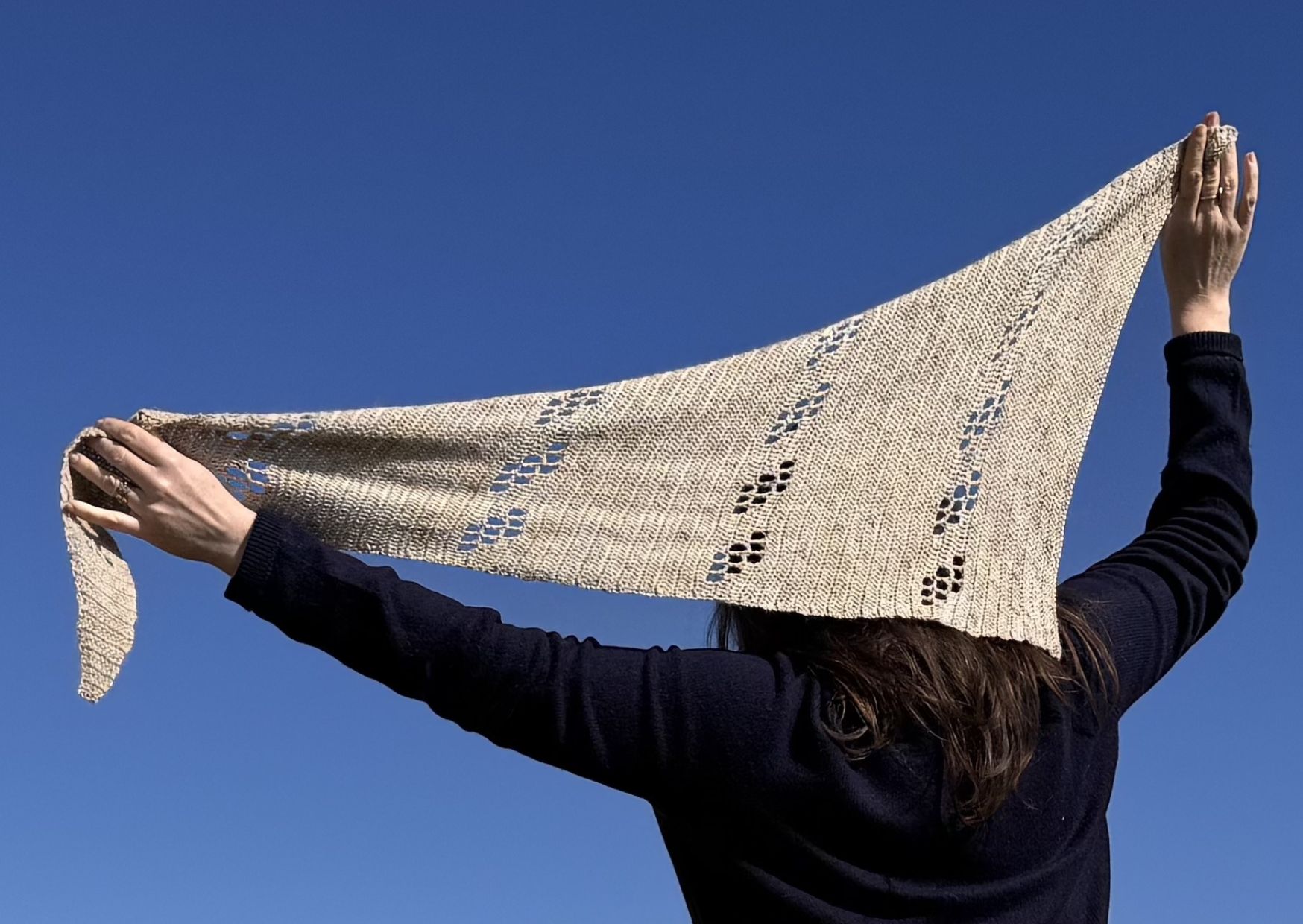 Asymetric crochet filet shawl being held up high against a blue sky.
