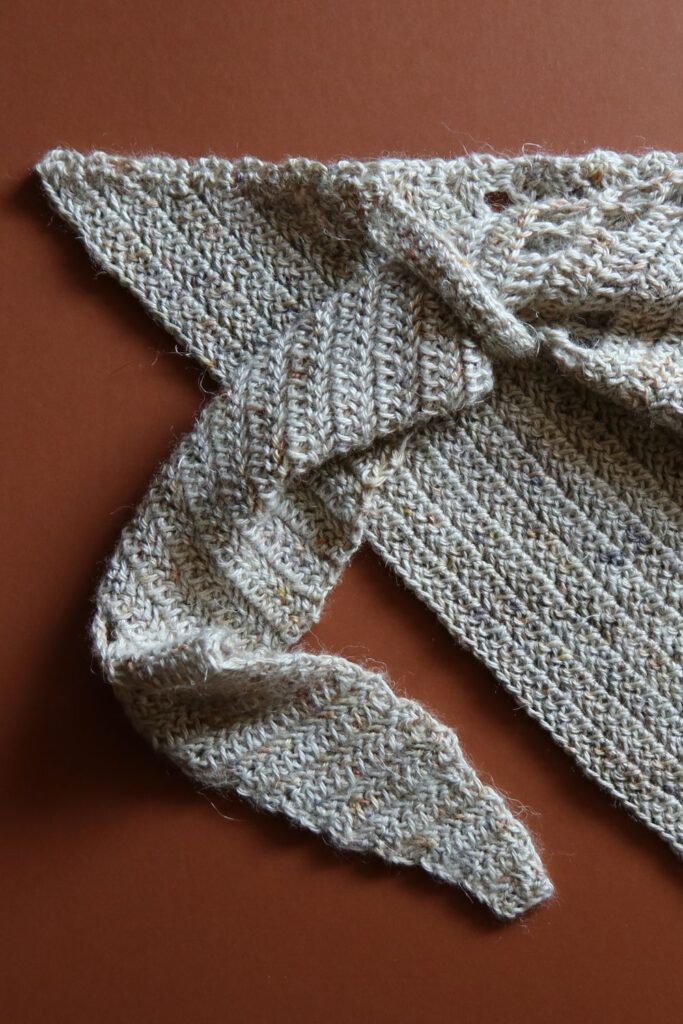 Close up of a crocheted shawl with a small tab with shawl end fed through to secure in place.