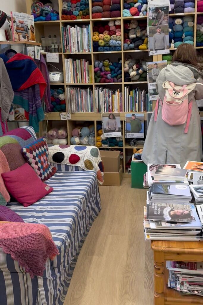 Sofa and table full of knitting books with yarn behind at Kathys Knits yarn shop in Edinburgh. 