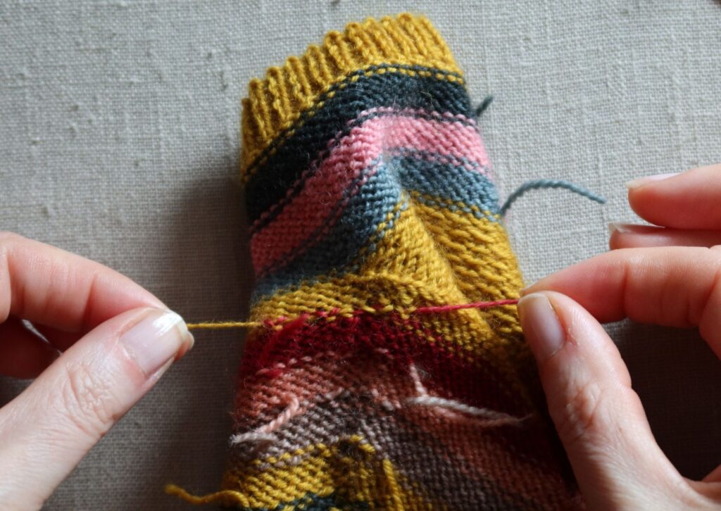 A pair of brightly coloured knitted striped trainer socks with no sew coloured yarn join method.