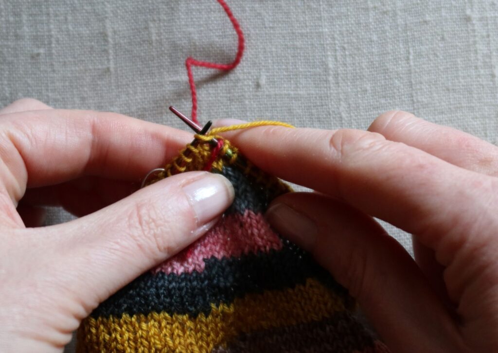 A pair of brightly coloured knitted striped trainer socks with no sew coloured yarn join method.