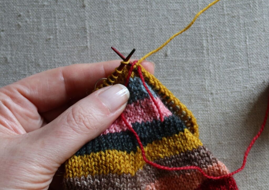 A pair of brightly coloured knitted striped trainer socks with no sew coloured yarn join method.