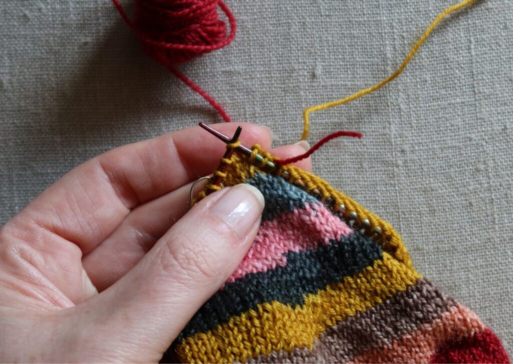 A pair of brightly coloured knitted striped trainer socks with no sew coloured yarn join method.